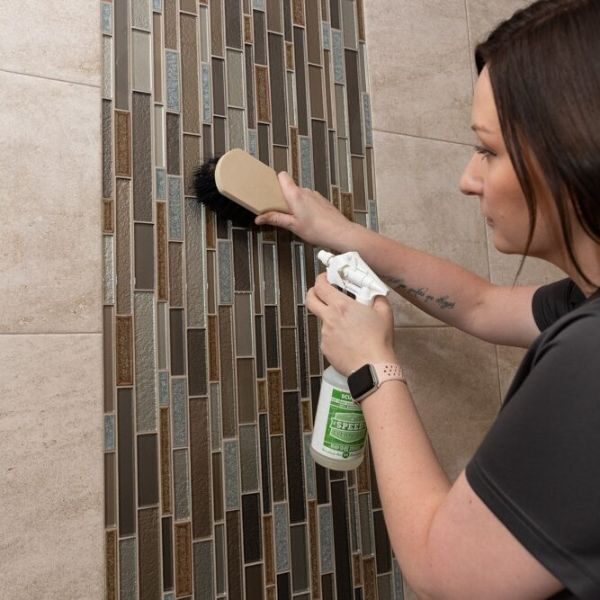 Housekeeper cleaning a shower with eco-friendly cleaning products.
